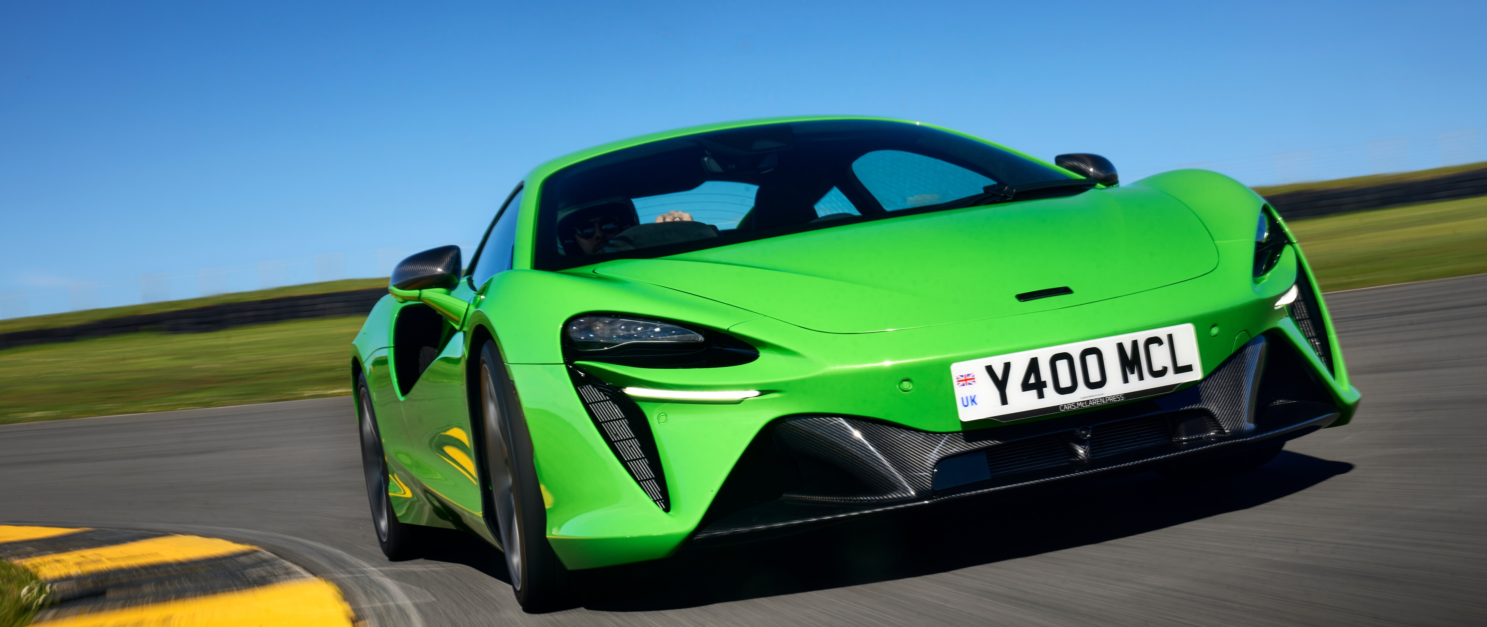 Une McLaren Artura, une voiture de sport de luxe d’un vert éclatant, dotée de lignes aérodynamiques et d’une finition brillante.